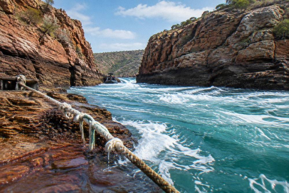 Turquoise water churning against layered rock walls in a narrow channel