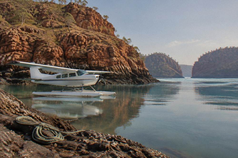 A seaplane resting on calm water beside a red rock coastline
