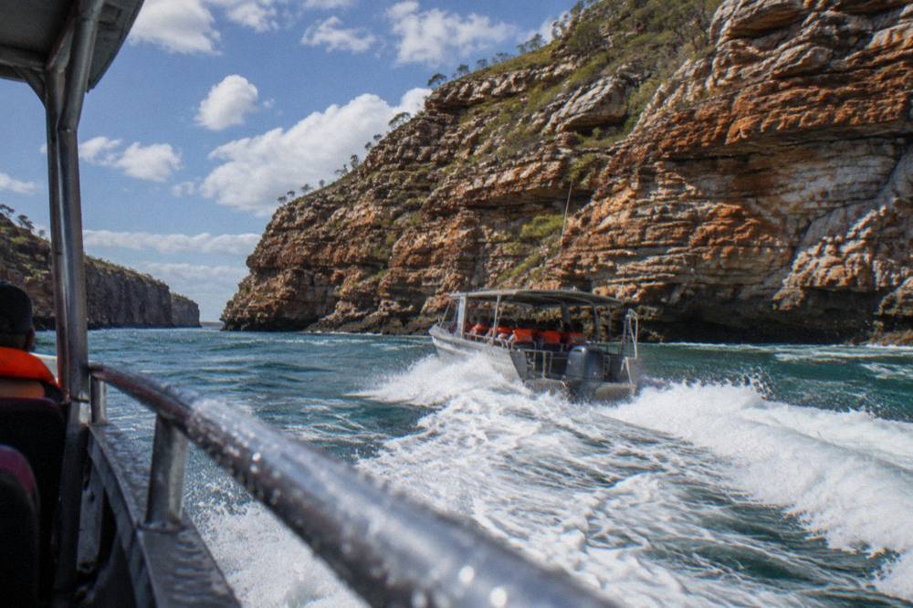A boat cutting through churned white water beside steep rock cliffs