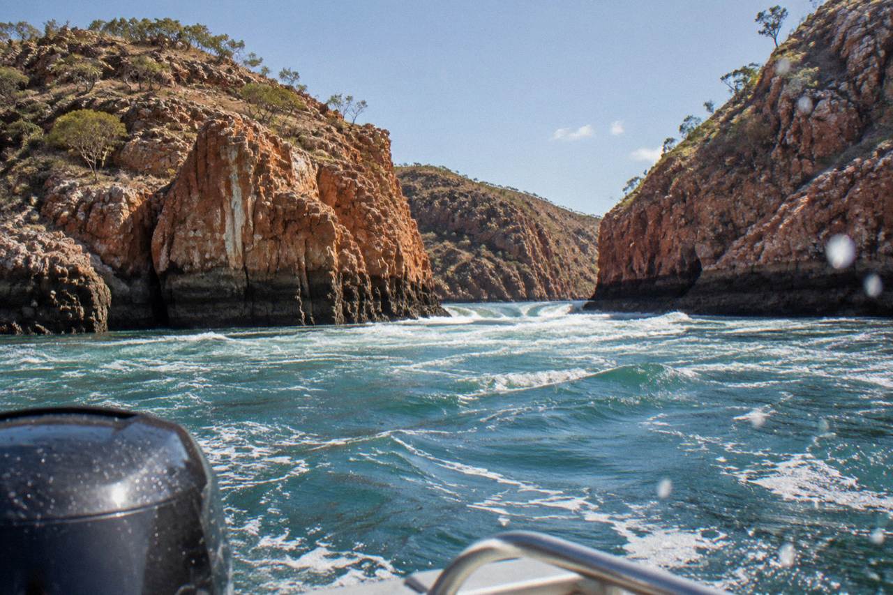 Turbulent water rushing through a narrow coastal gorge between red rock cliffs