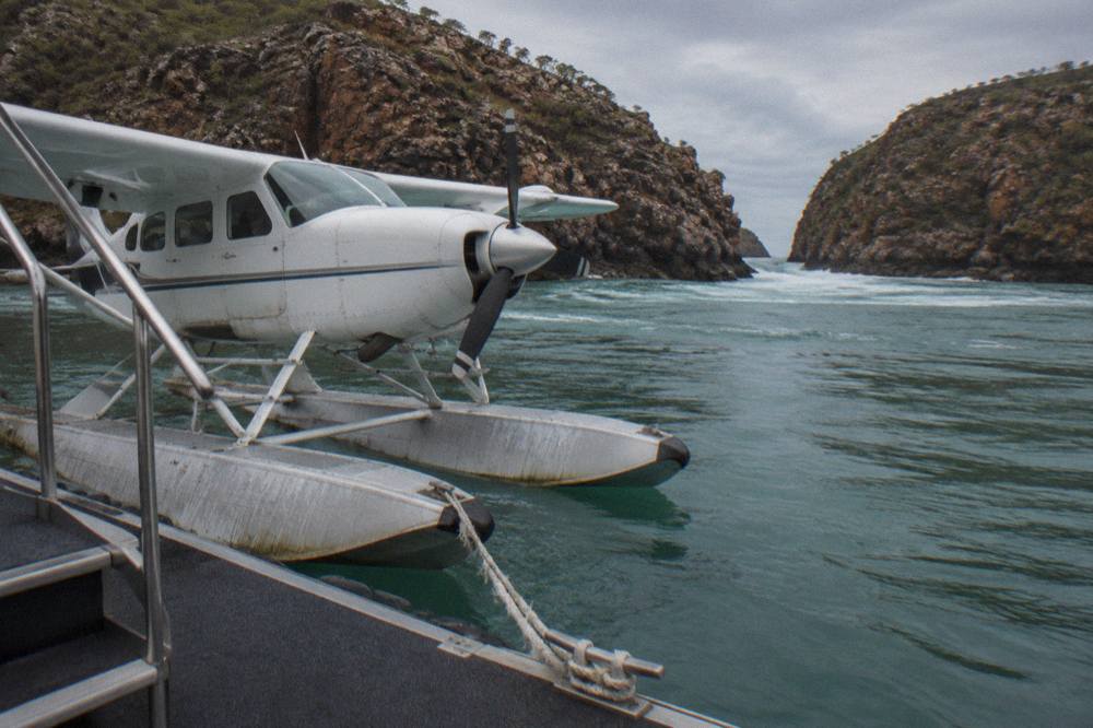 A seaplane floating beside a pontoon at Talbot Bay with dark cliffs and tidal water around it