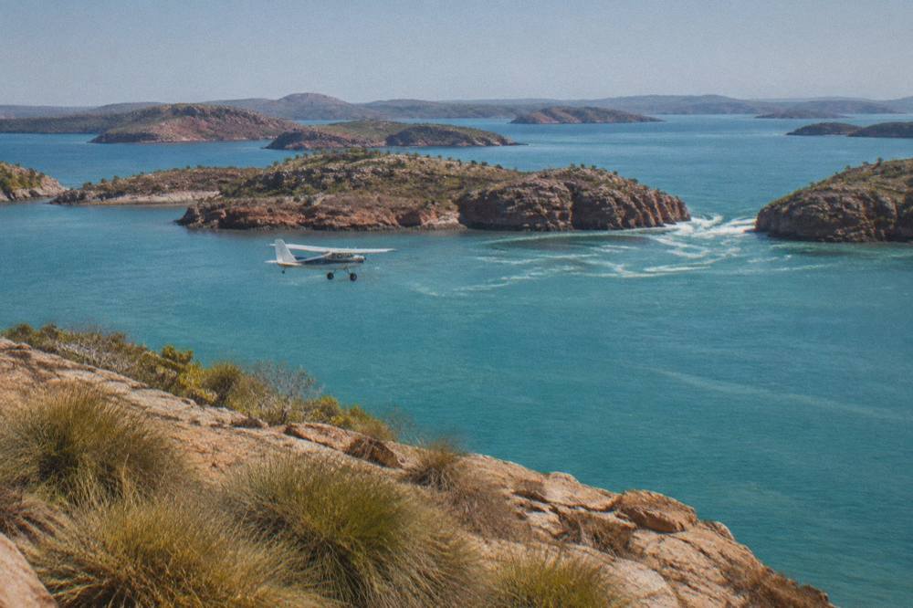 A light aircraft flying over turquoise water and scattered rocky islands