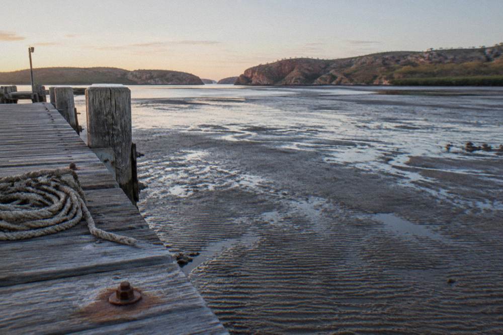 A long wooden jetty extending over wide mudflats at low tide