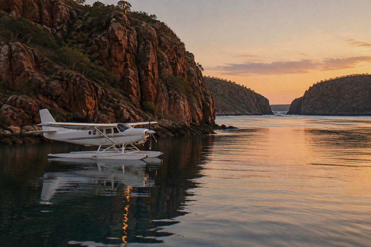 A seaplane resting on calm water beside rugged red cliffs in Talbot Bay