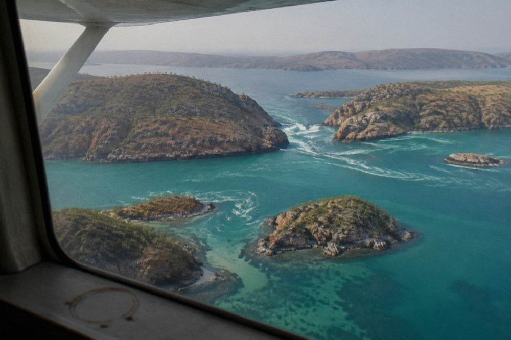 Light aircraft banking over scattered rocky islands in clear turquoise sea