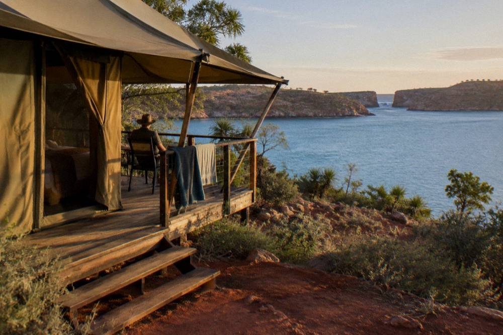 Safari-style canvas tent on a wooden deck overlooking calm turquoise bay water