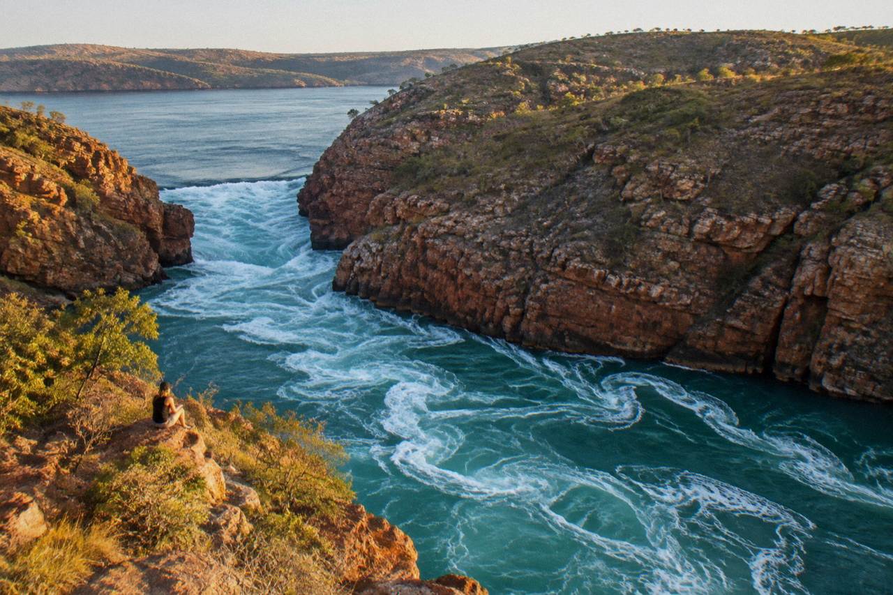 Aerial view of turbulent water rushing through two narrow coastal gorges in red rock cliffs