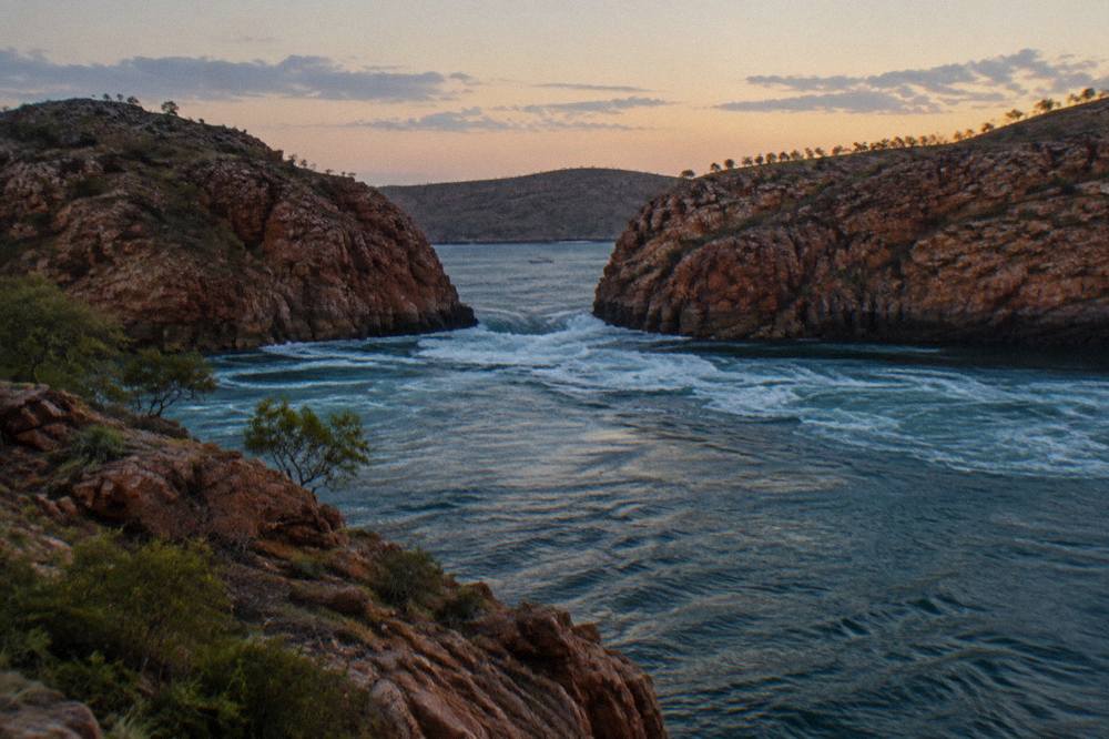 White water surging through a narrow sandstone channel between red rock cliffs in Talbot Bay