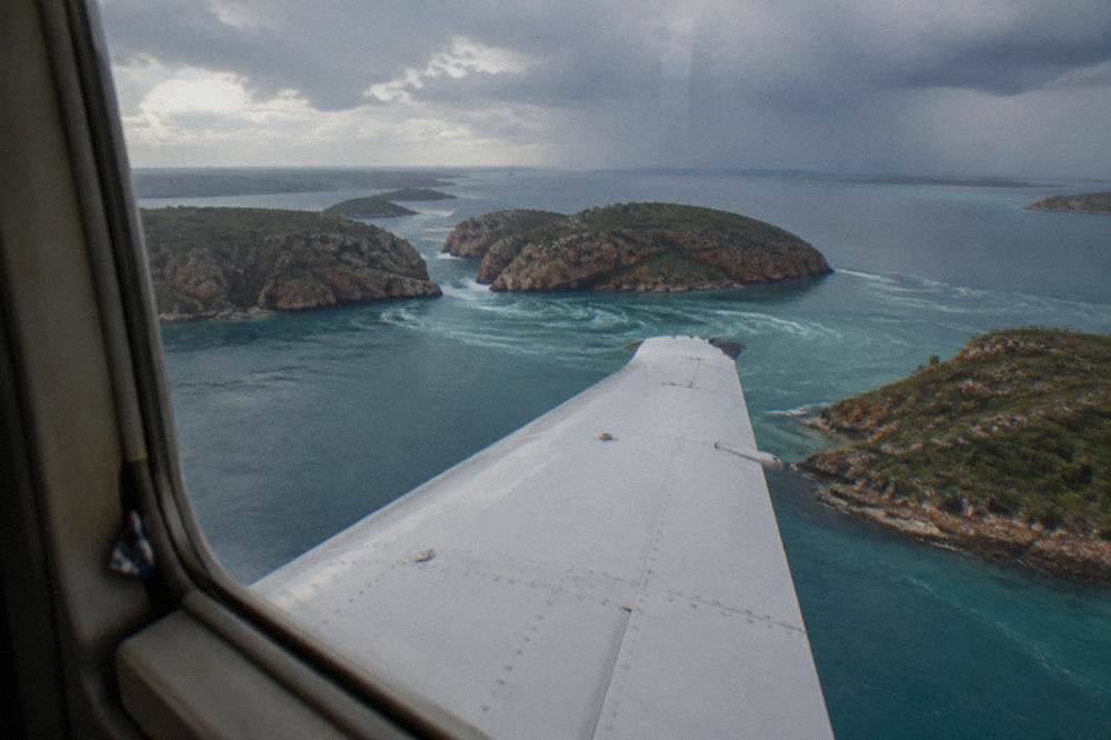 A light aircraft wing above turquoise water and scattered rocky islands of the Buccaneer Archipelago