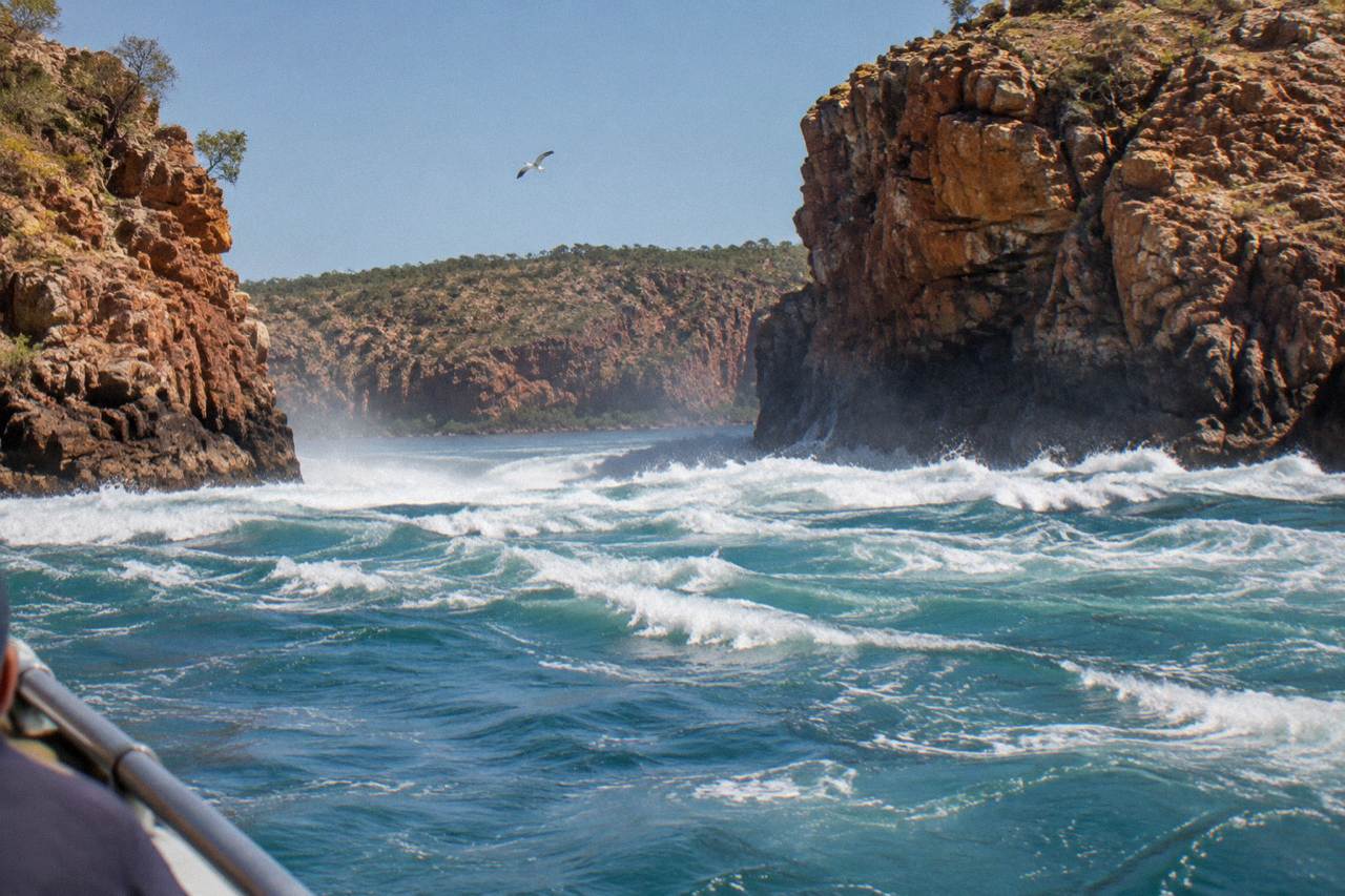 Turbulent tidal water rushing through a narrow red rock gap in Talbot Bay under a clear sky