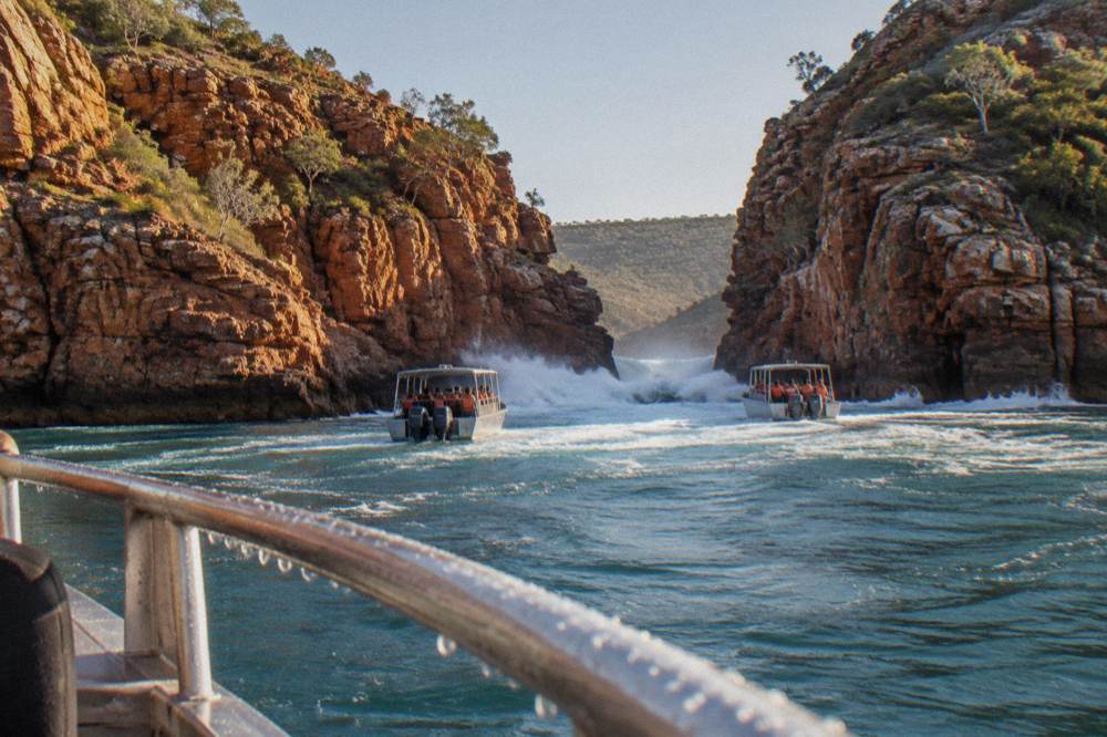 Small tender boats holding passengers close to white water rushing through a narrow red rock channel