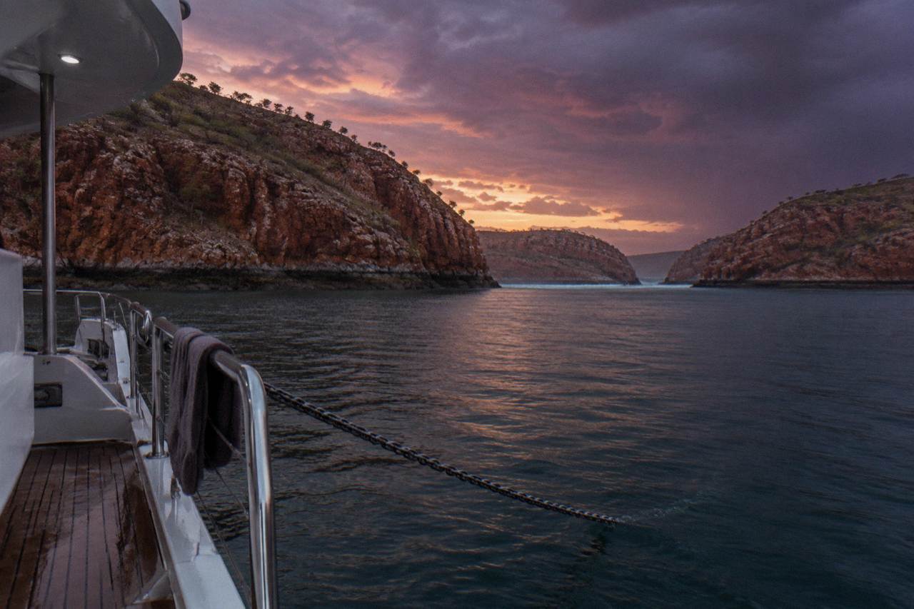 A cruise vessel anchored in a red rock bay surrounded by steep sandstone cliffs at sunset