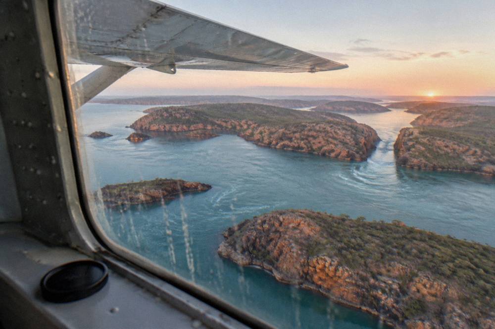 A light aircraft wing above island-dotted turquoise water in the Buccaneer Archipelago
