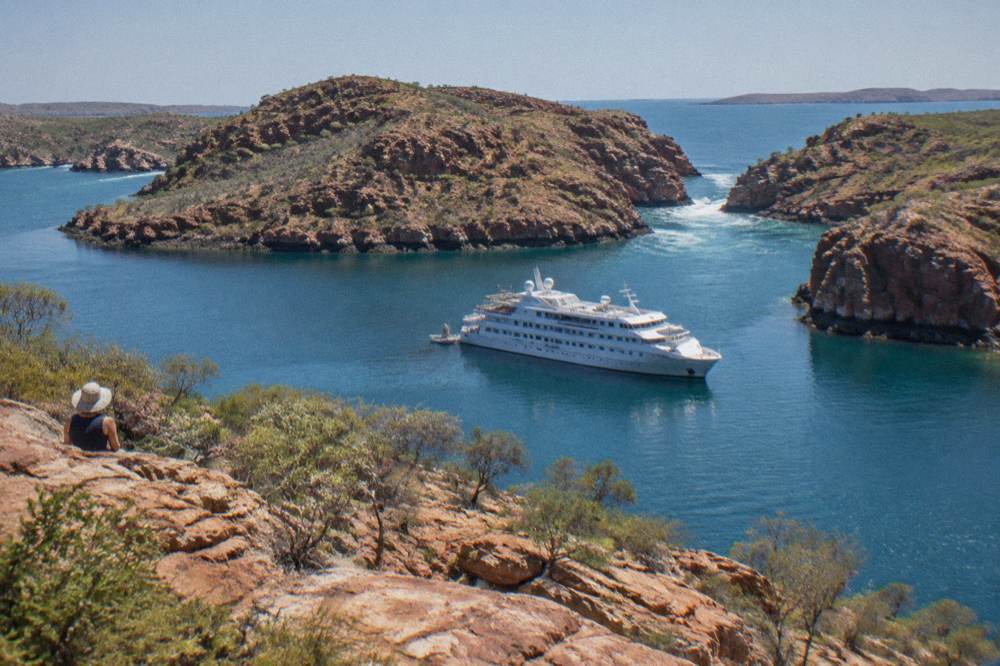 A cruise vessel anchored near red rock islands in calm blue water
