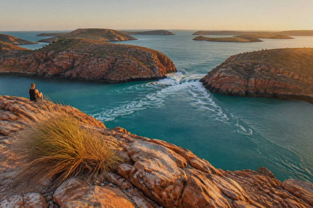 A red cliff coastline with turquoise water and scattered rocky islands under a clear sky