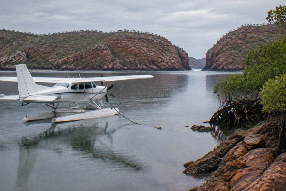 A seaplane floating on calm turquoise water beside a red rock shoreline