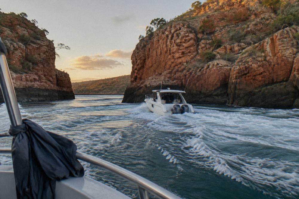 A white power boat cutting through turbulent whitewater between steep rock walls