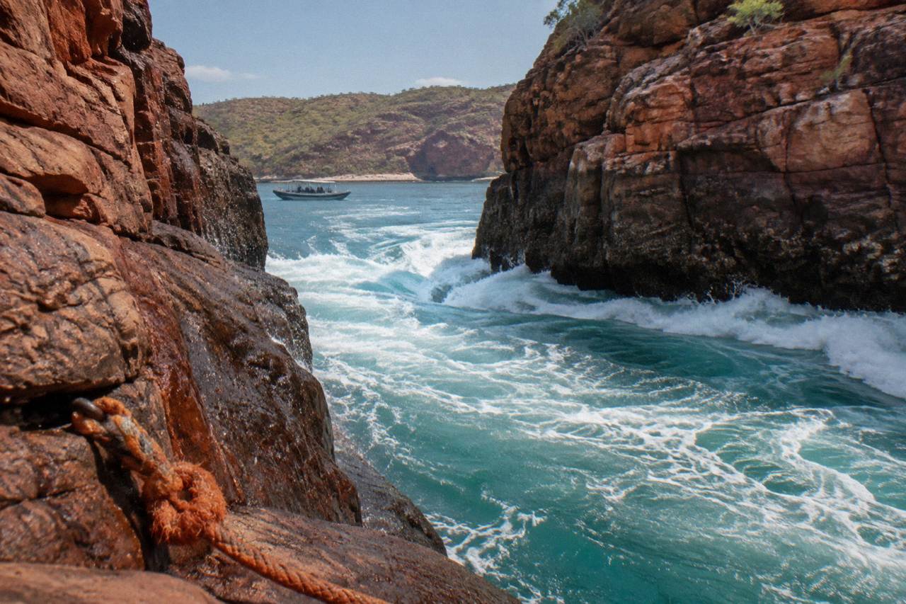 Turquoise water rushing through a narrow rocky gap in red cliffs at Talbot Bay