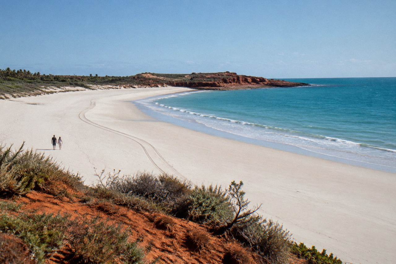 Wide empty beach with red sand cliffs and turquoise water under a clear sky
