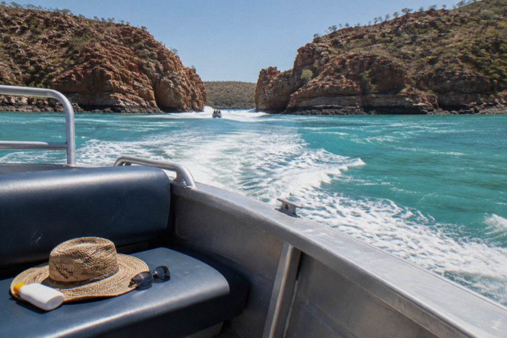 A straw hat and polarised sunglasses resting on a boat seat beside a sunscreen bottle