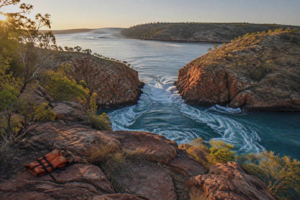 Two parallel narrow channels of turbulent water cutting through a red cliff range in a remote bay