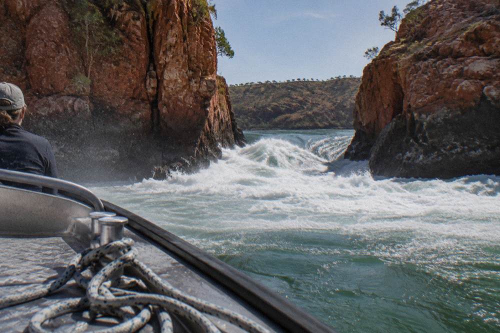 Rushing white water squeezing through a narrow rock channel and dropping to a calmer sea beyond