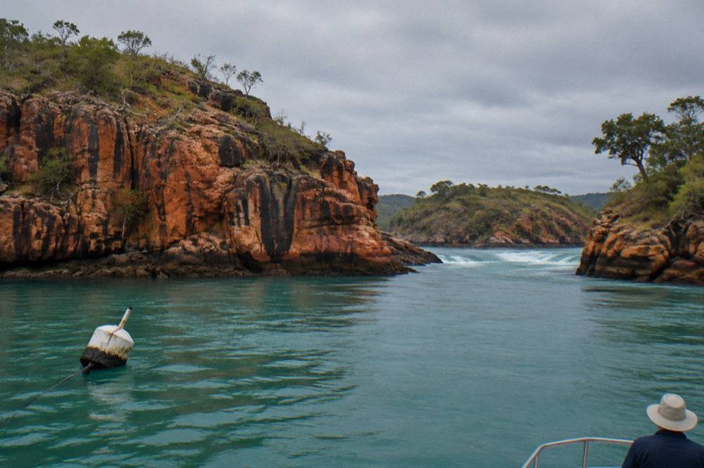 Red sandstone cliffs rising from clear green water with small wooded islands in the distance