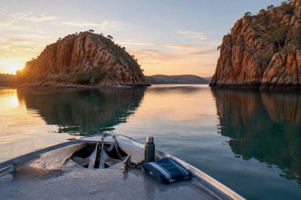 A small boat crossing flat calm water between steep rock islands at sunrise