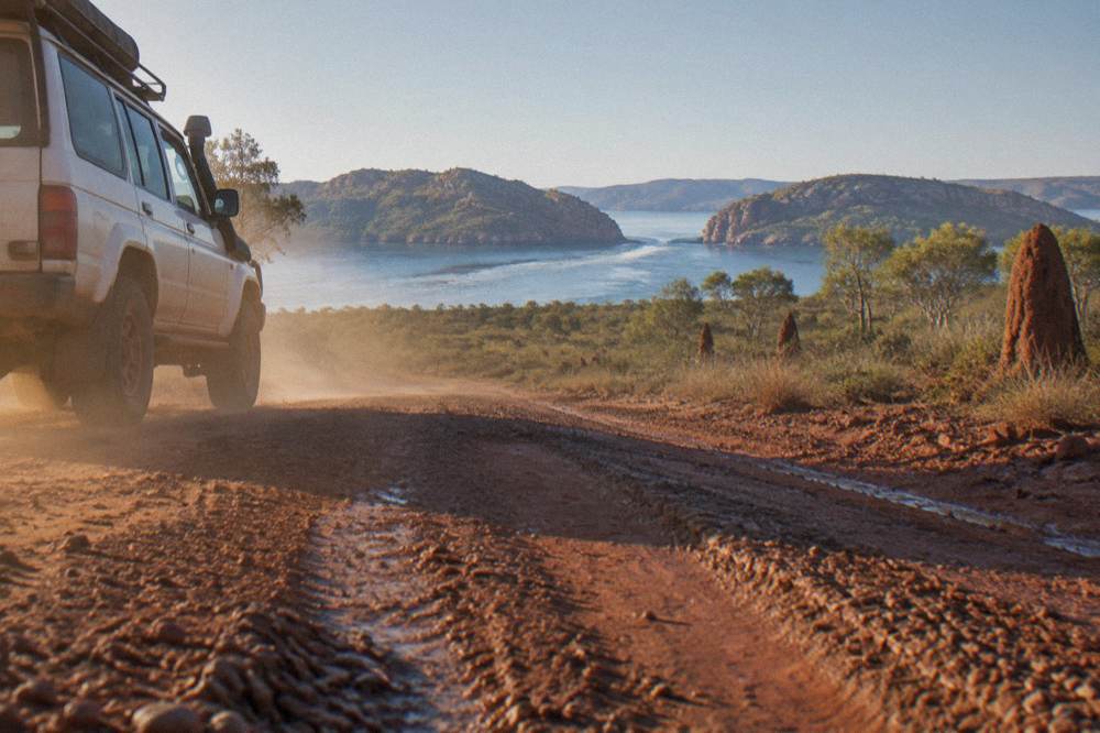 Four wheel drive tour vehicle on a red dirt road lined with pindan scrub at sunrise